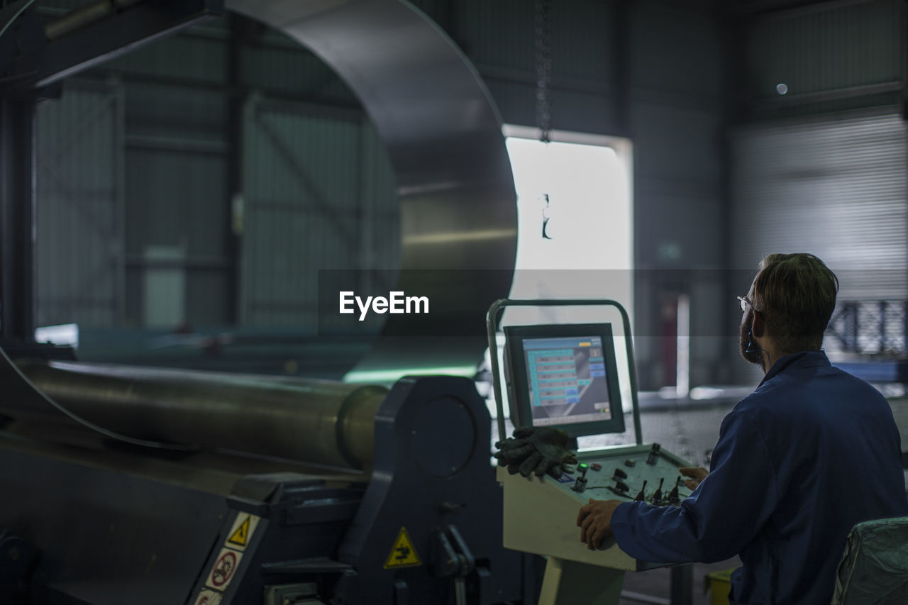 Worker operating machinery at control panel in steel factory