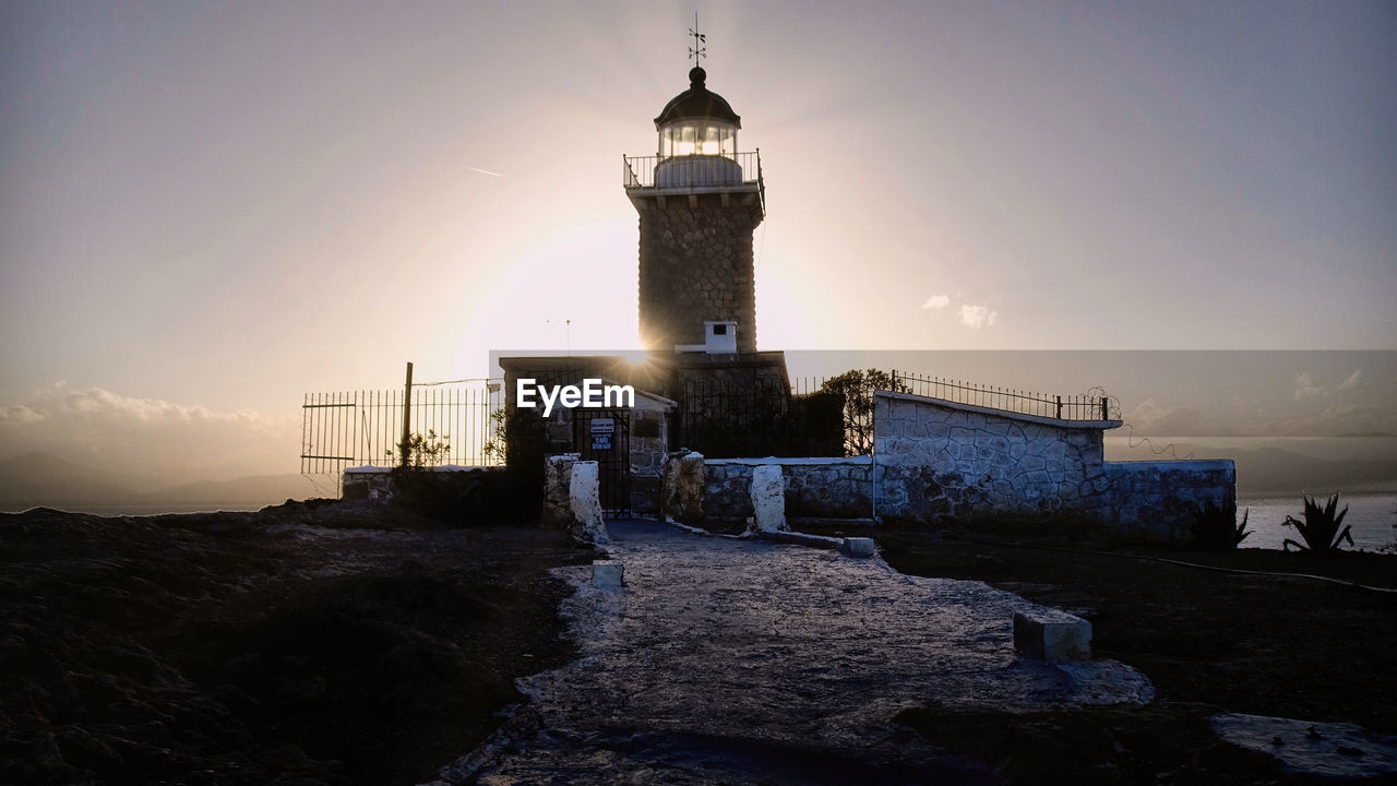 Lighthouse by sea against sky during sunset