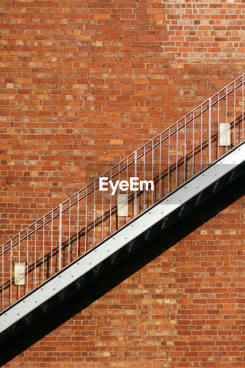 An empty fire escape stairs on the building exterior, red brick wall background.