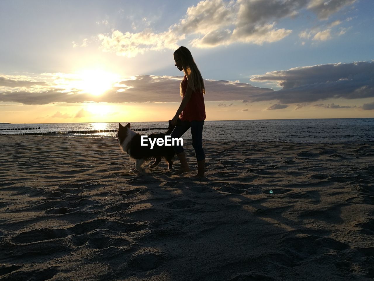 Woman with dog at beach against sky during sunset