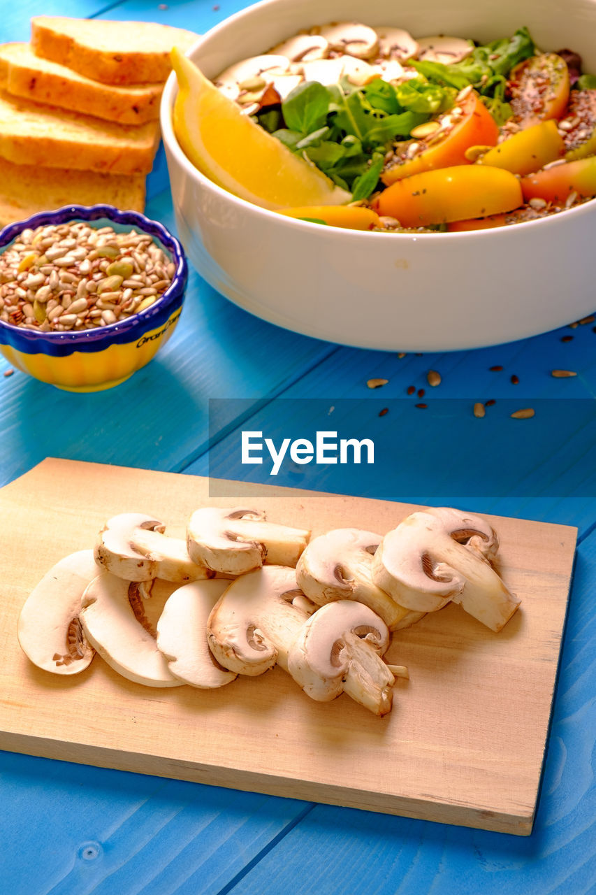 Top view of a bowl of mixed salad with tomatoes, mushrooms, lettuce and seeds with bread 