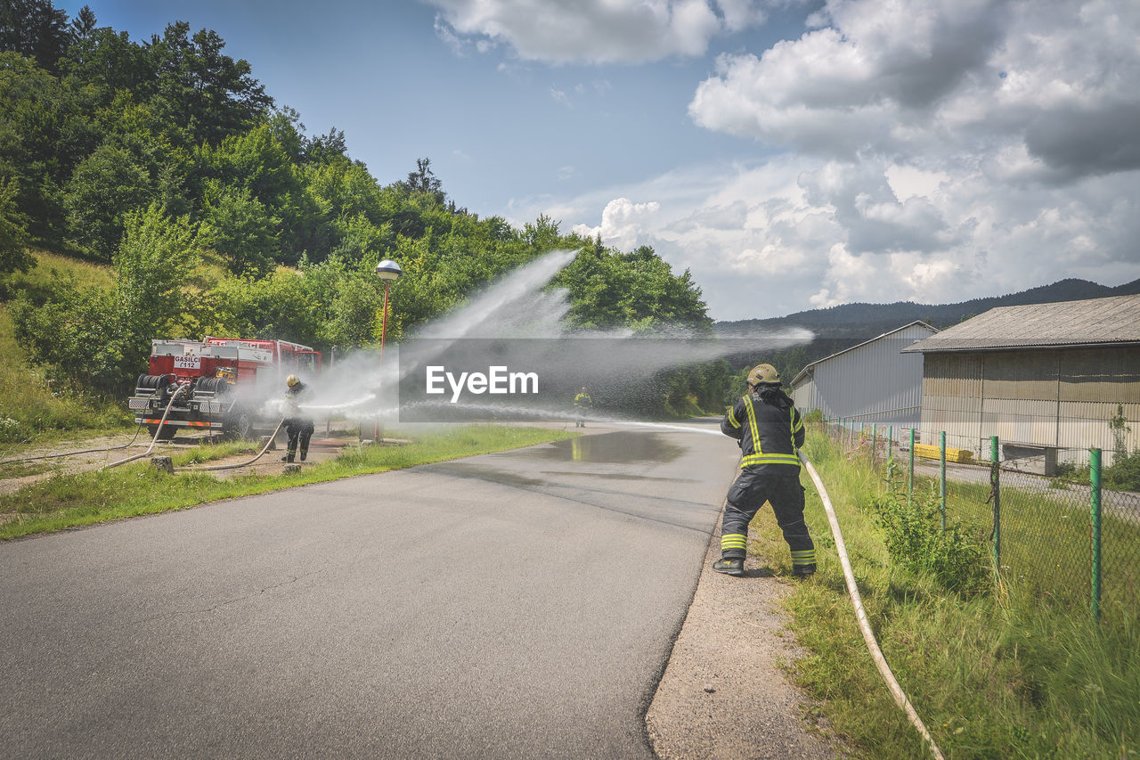 Firefighter spraying water on road against cloudy sky