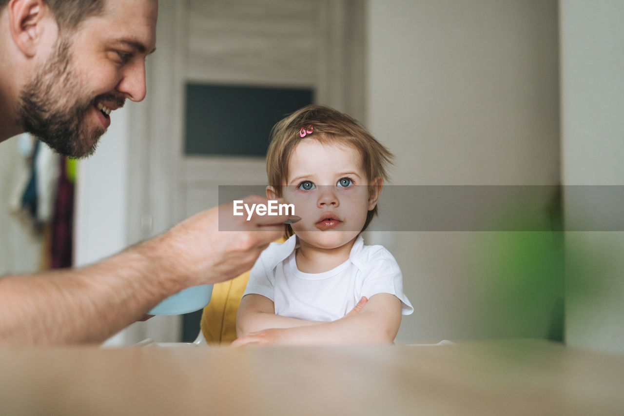 Father young man feeds baby girl little daughter in kitchen at home