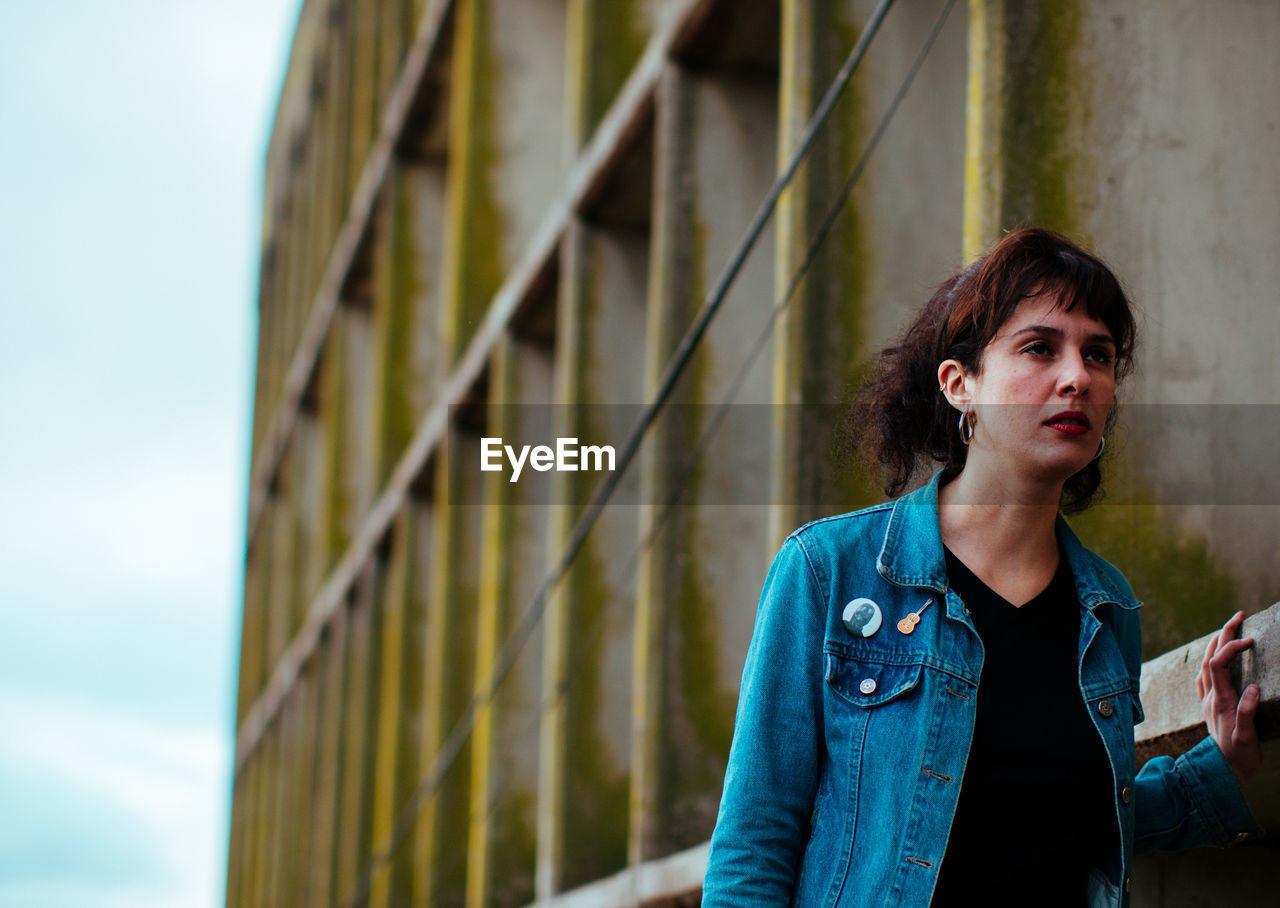 Woman looking away while standing by wall