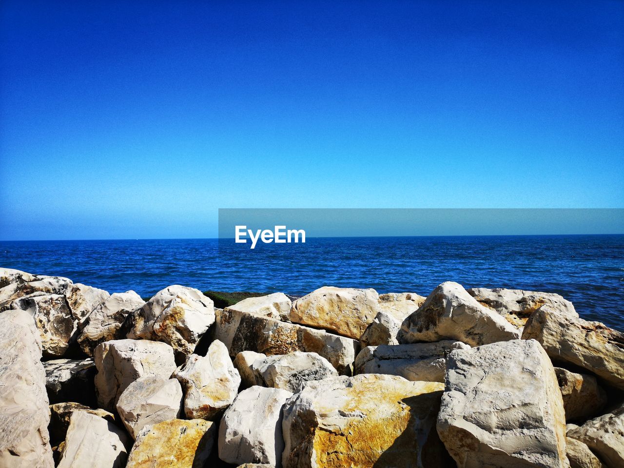 Rocks by sea against clear blue sky