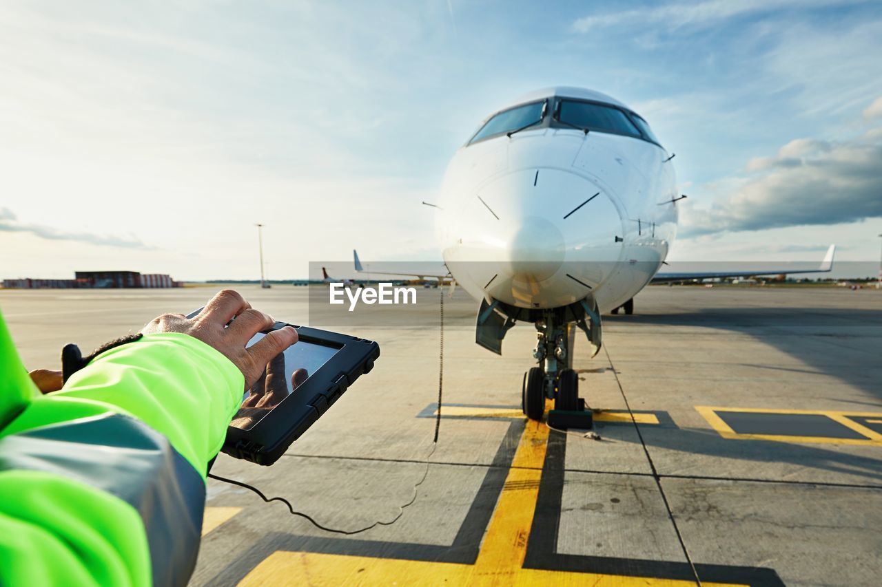 Cropped hands of man using digital tablet against airplane at runway