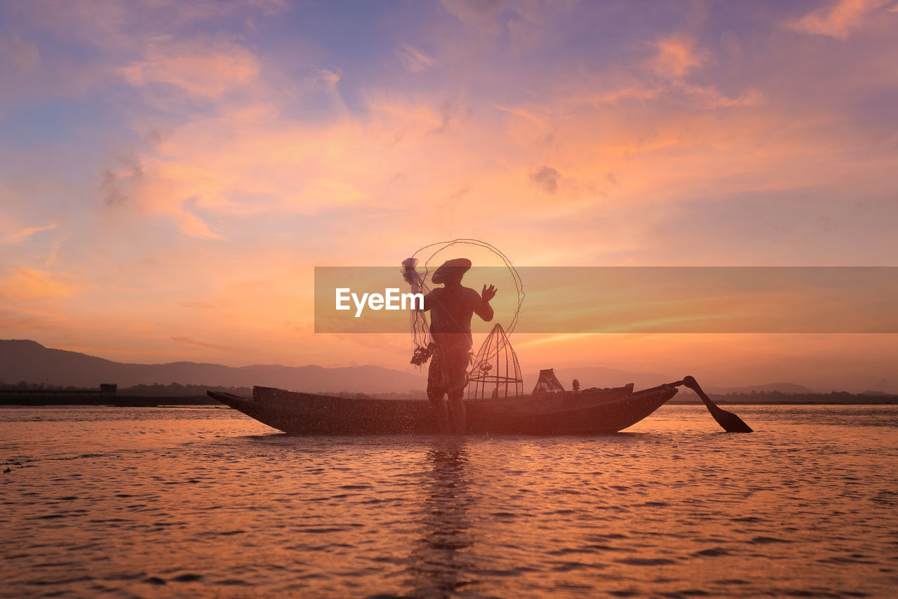 Silhouette fisherman fishing in sea against cloudy sky during sunset