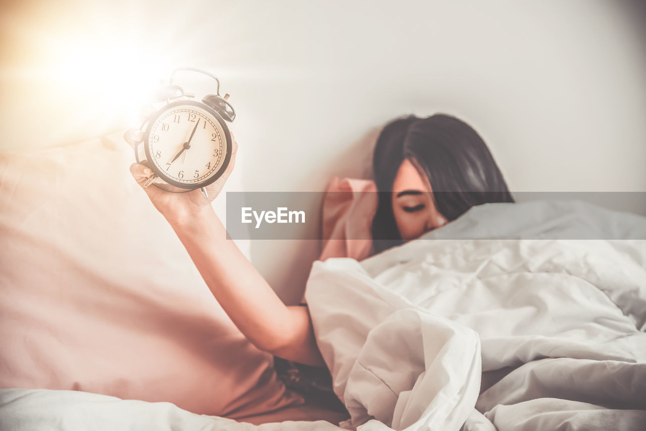 Sleepy woman holding alarm clock on bed