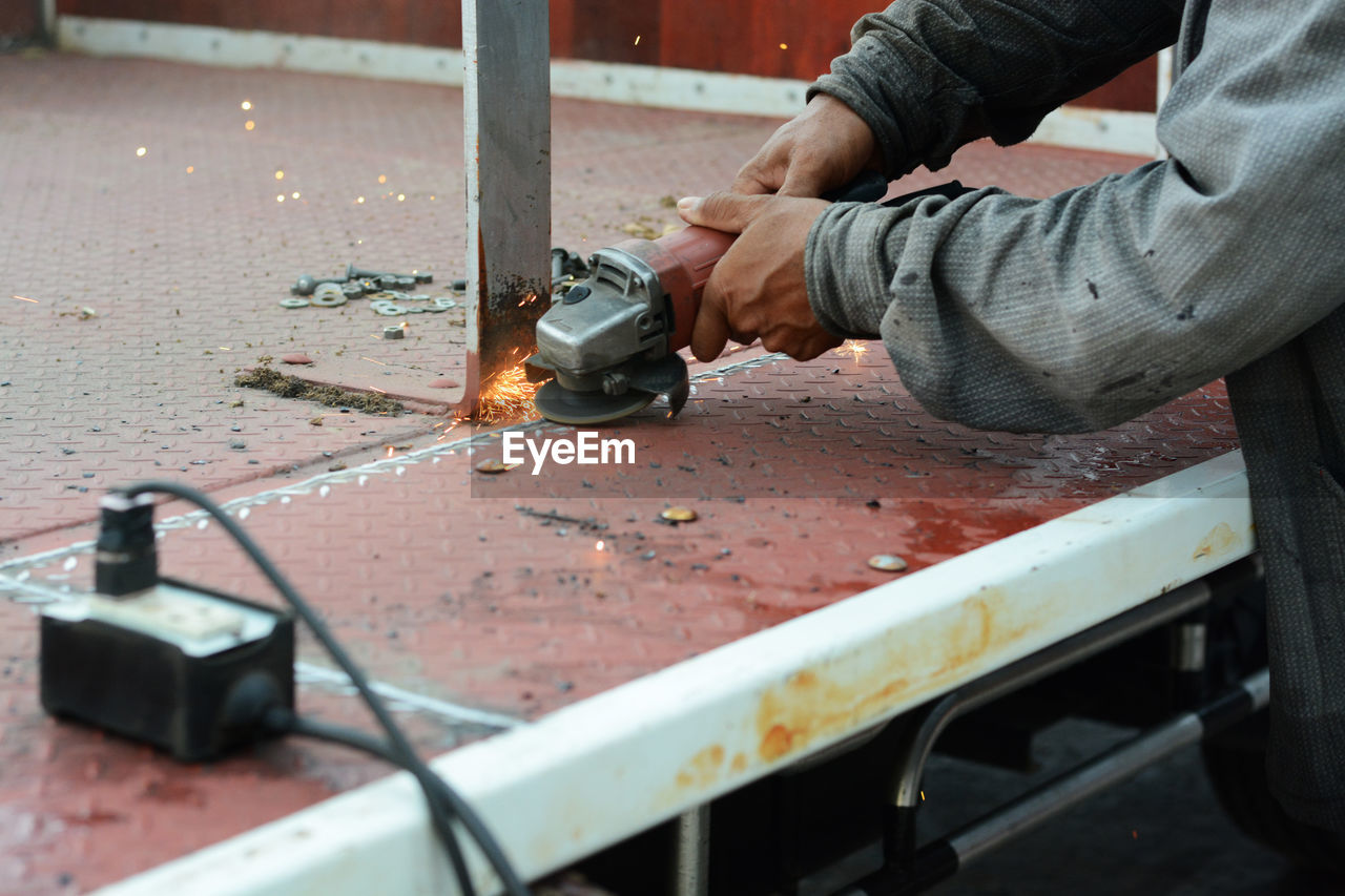 Midsection of worker cutting metal with power tool