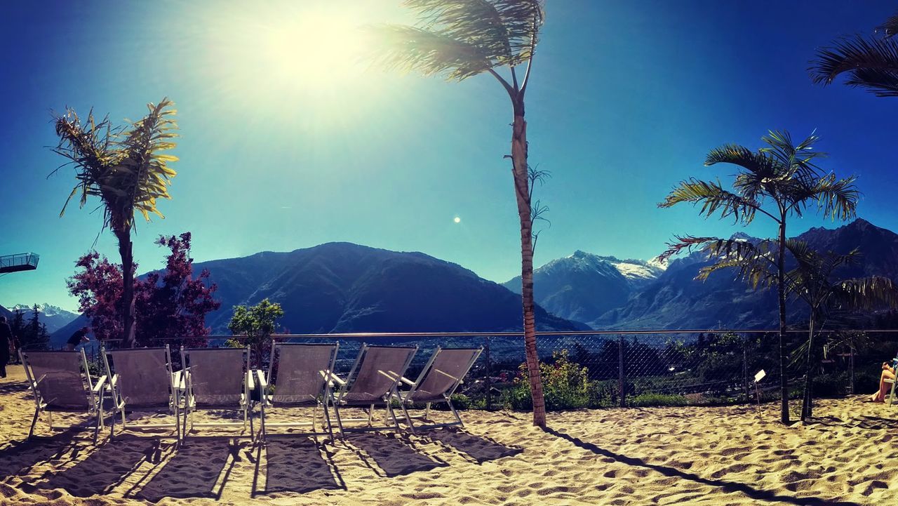 Empty lounge chairs by tree on sunny day against sky