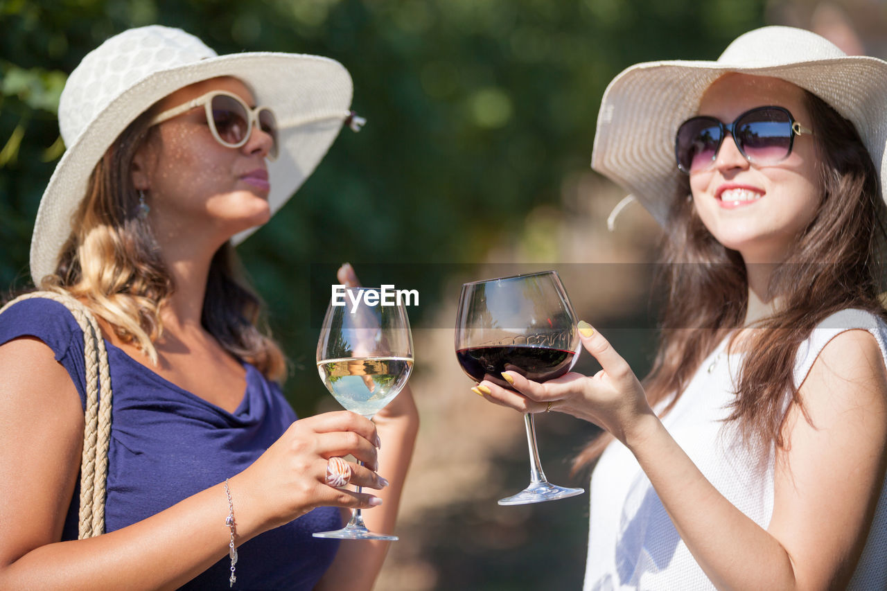 Young woman wearing sunglasses while holding wineglasses outdoors