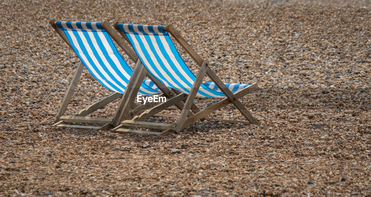 Two blue and white striped deckchairs on a pebble beach
