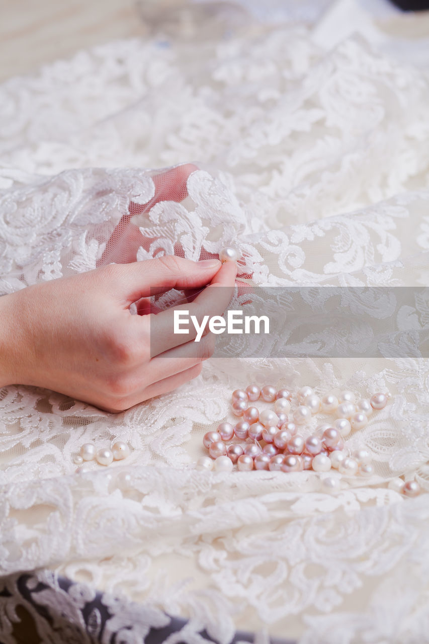 Cropped hand of woman stitching pearls on white wedding dress