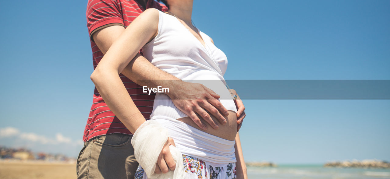 Midsection of man holding pregnant woman belly at beach