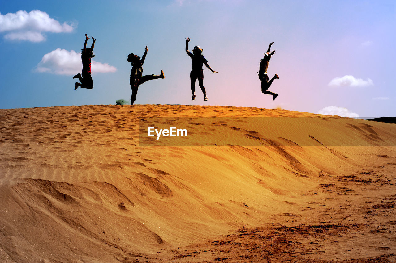 Full length of women jumping on sand dune in desert against sky