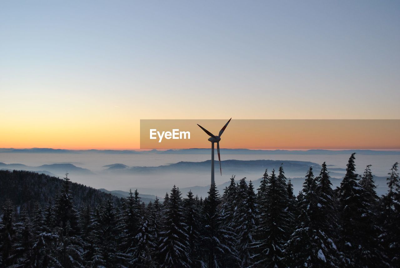 Windmill in forest against sky during sunset