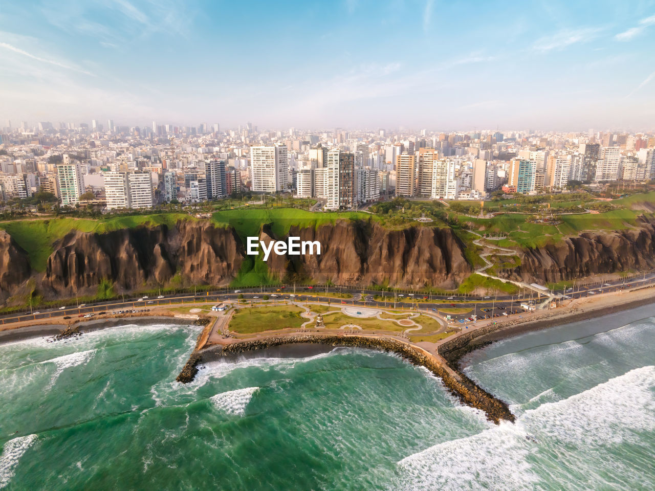 Breathtaking aerial view of wavy ocean washing sandy coastline near modern residential and commercial building against cloudy blue sky in lima