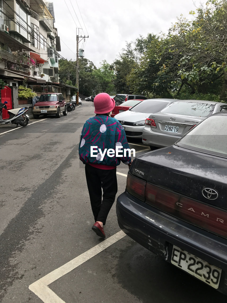 REAR VIEW OF WOMAN WITH UMBRELLA STANDING IN CAR