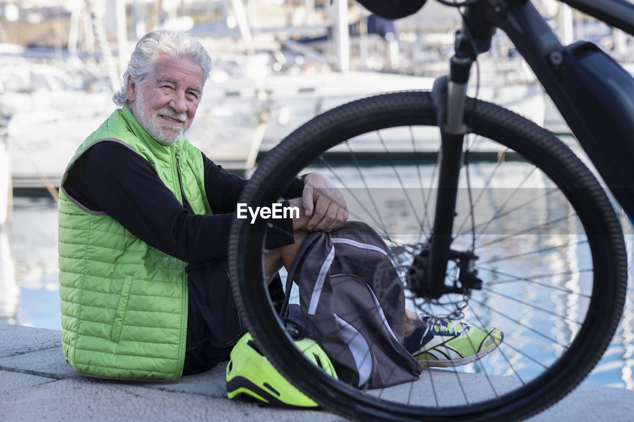 Portrait of man sitting by bicycle at harbor