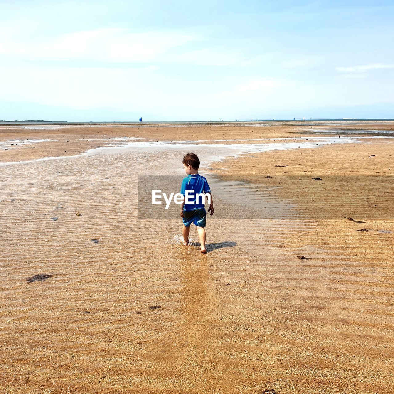 Rear view of boy walking at beach against sky