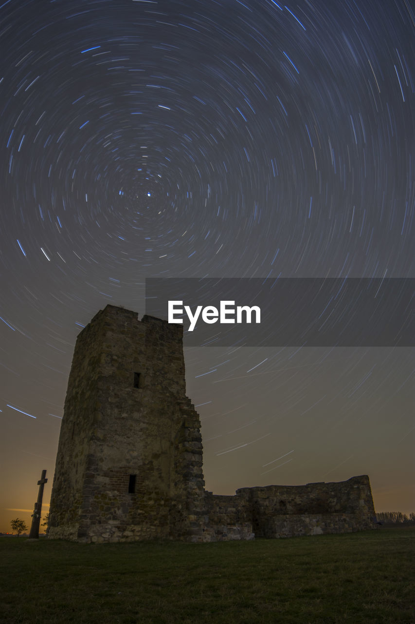 Low angle view of historic building against star trails at night