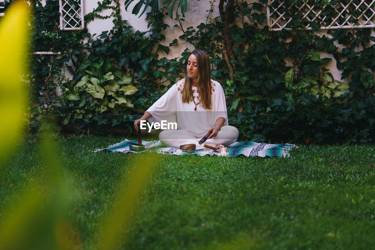 WOMAN SITTING IN YARD AGAINST PLANTS