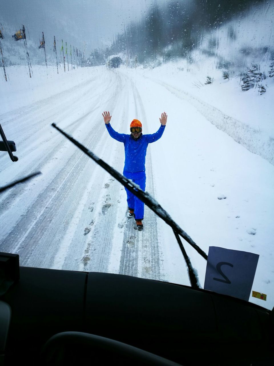 Man with arms raised standing against bus during winter seen through windshield