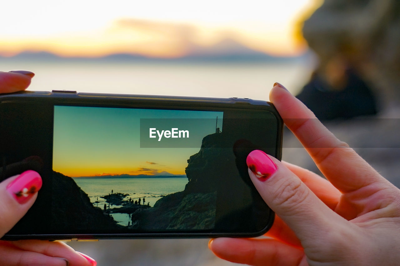 Cropped hands of woman photographing with mobile phone during sunset