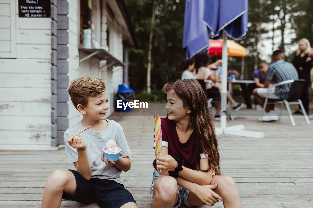 Smiling brother and sister eating sweet food while sitting on wooden floor