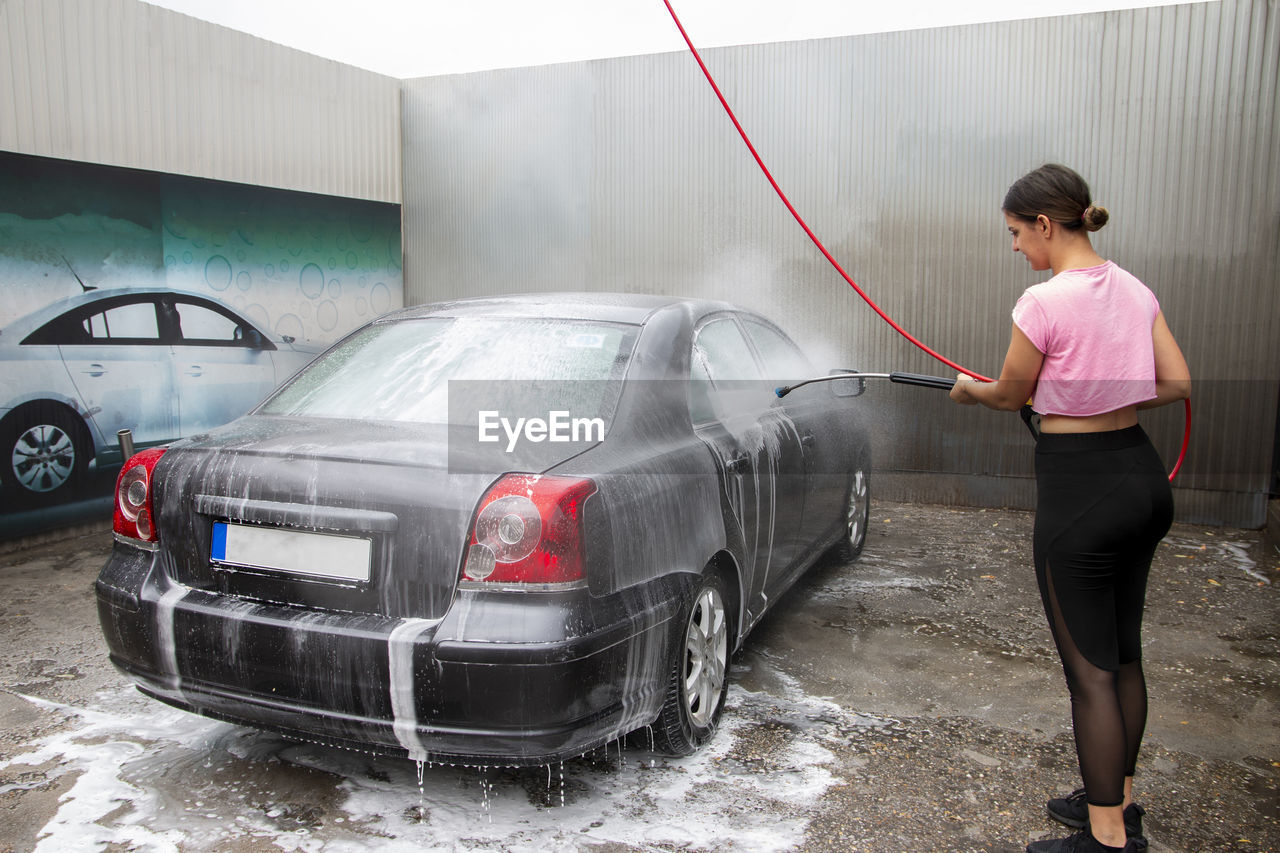 Cute teenager girl cleaning automobile with covered with foam shampoo chemical detergents