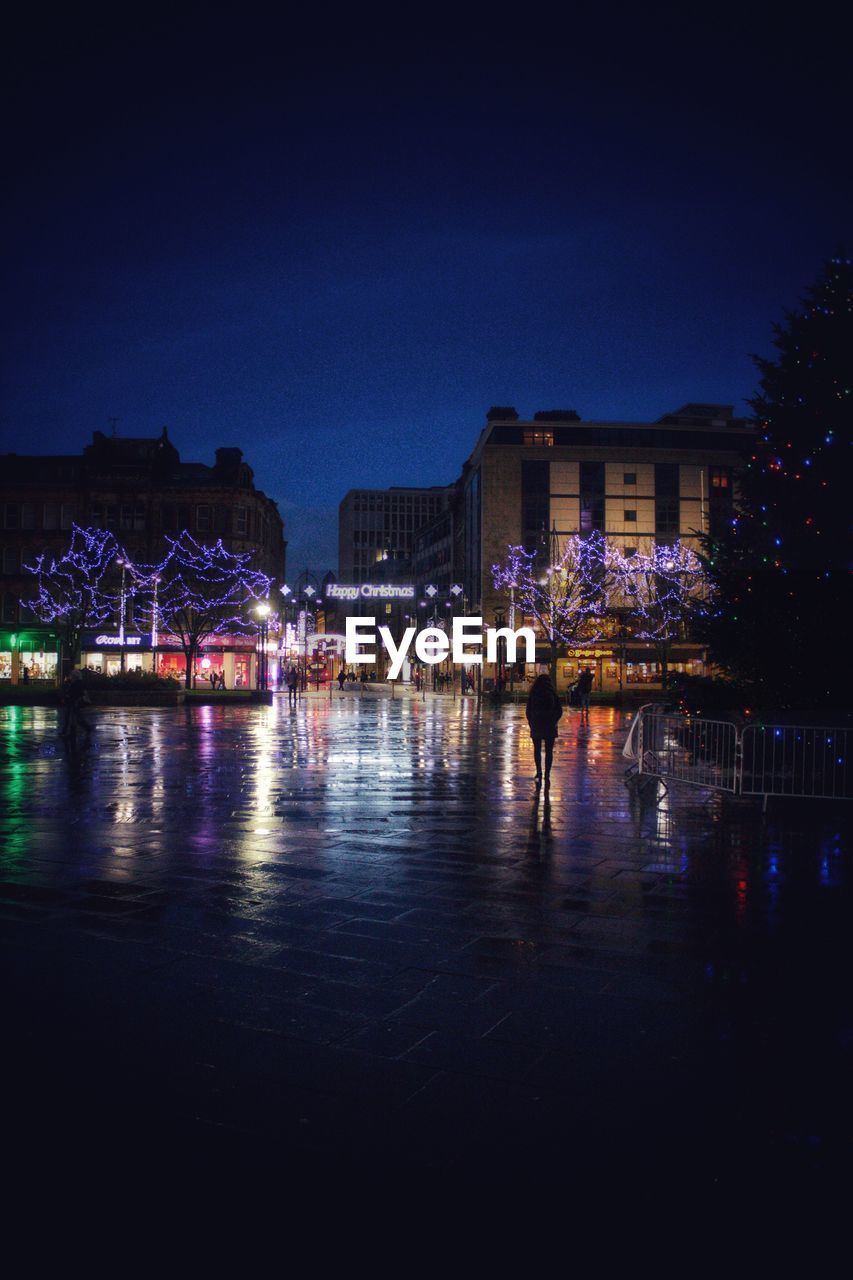 ILLUMINATED CITYSCAPE BY WATER AGAINST SKY AT NIGHT