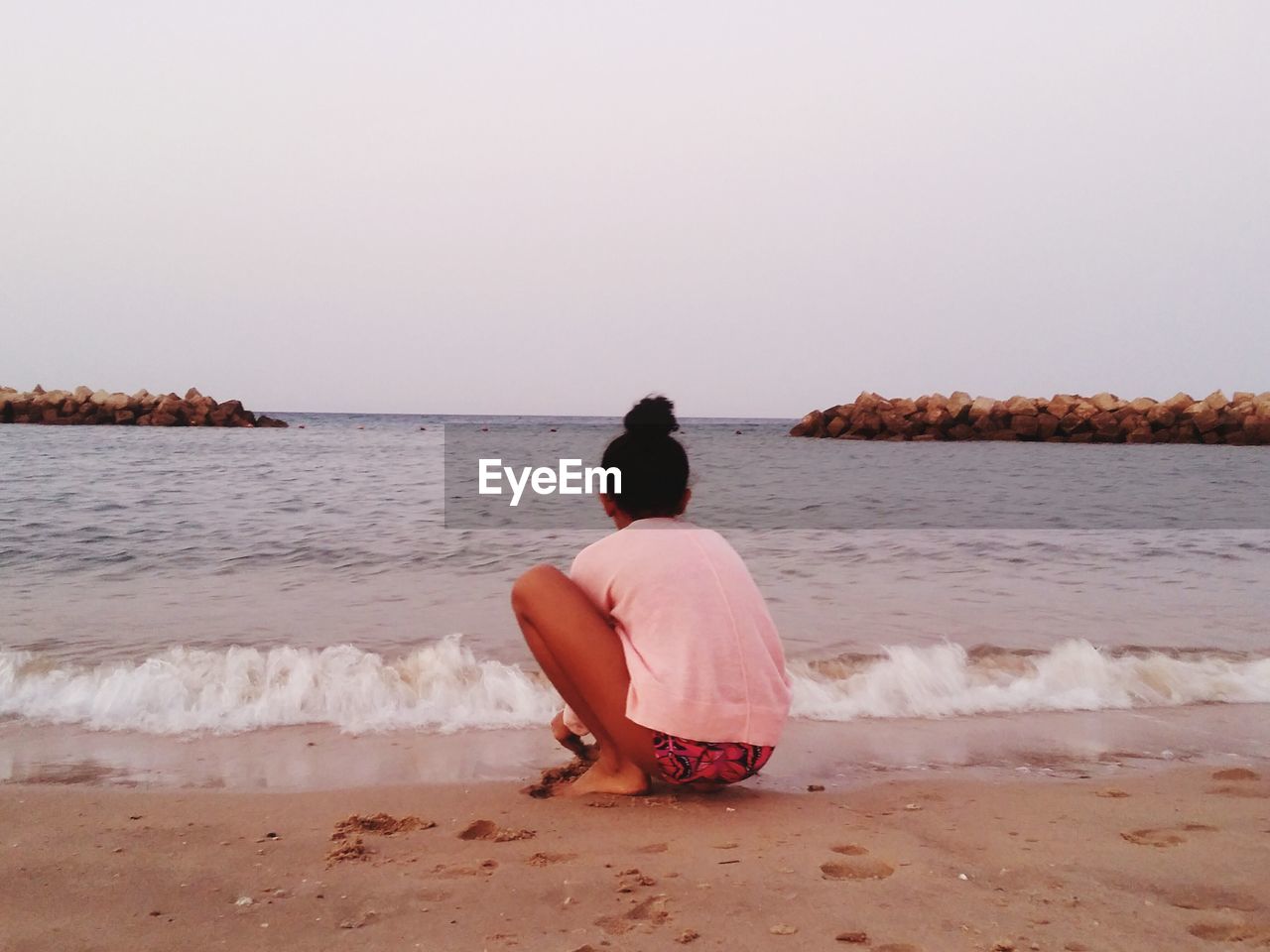 Rear view of girl sitting on beach against clear sky