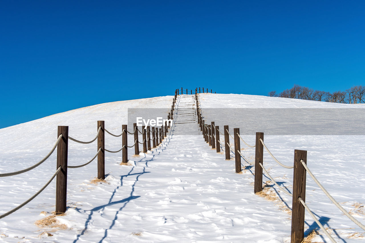 Wooden posts in snow against clear blue sky