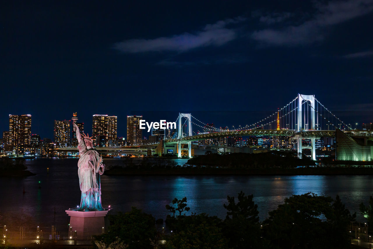 View of rainbow bridge and statue of liberty in odaiba, japan at night