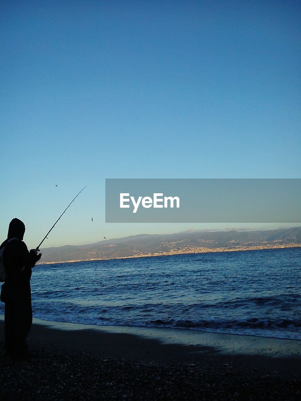 MAN FISHING AT BEACH AGAINST CLEAR SKY