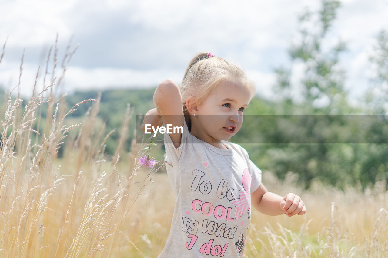 Cute girl standing amidst plants on field