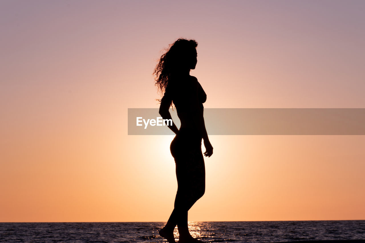 Silhouette woman walking by sea against clear sky during sunset