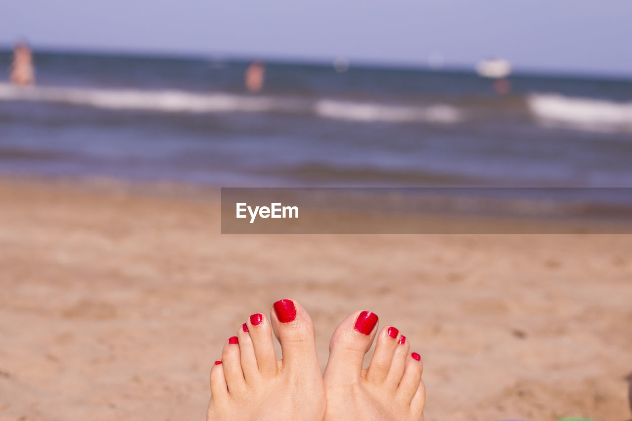 Low section of woman with red nail polish at beach