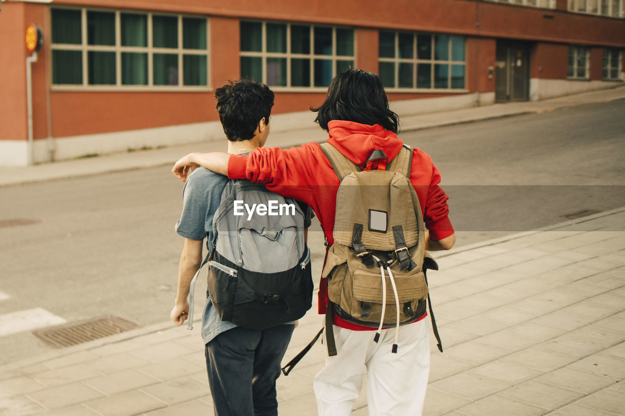 Rear view of friends with backpacks walking on street in city