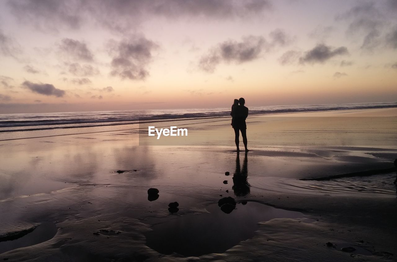 Person holding a child on beach at sunset