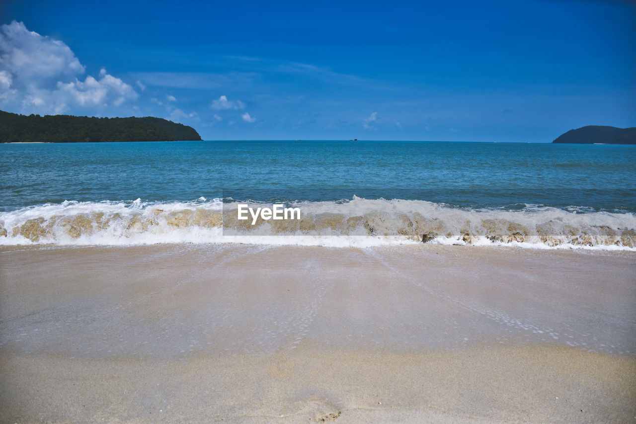Waves of the azure andaman sea under the blue sky reaching the shores of cenang beach in langkawi