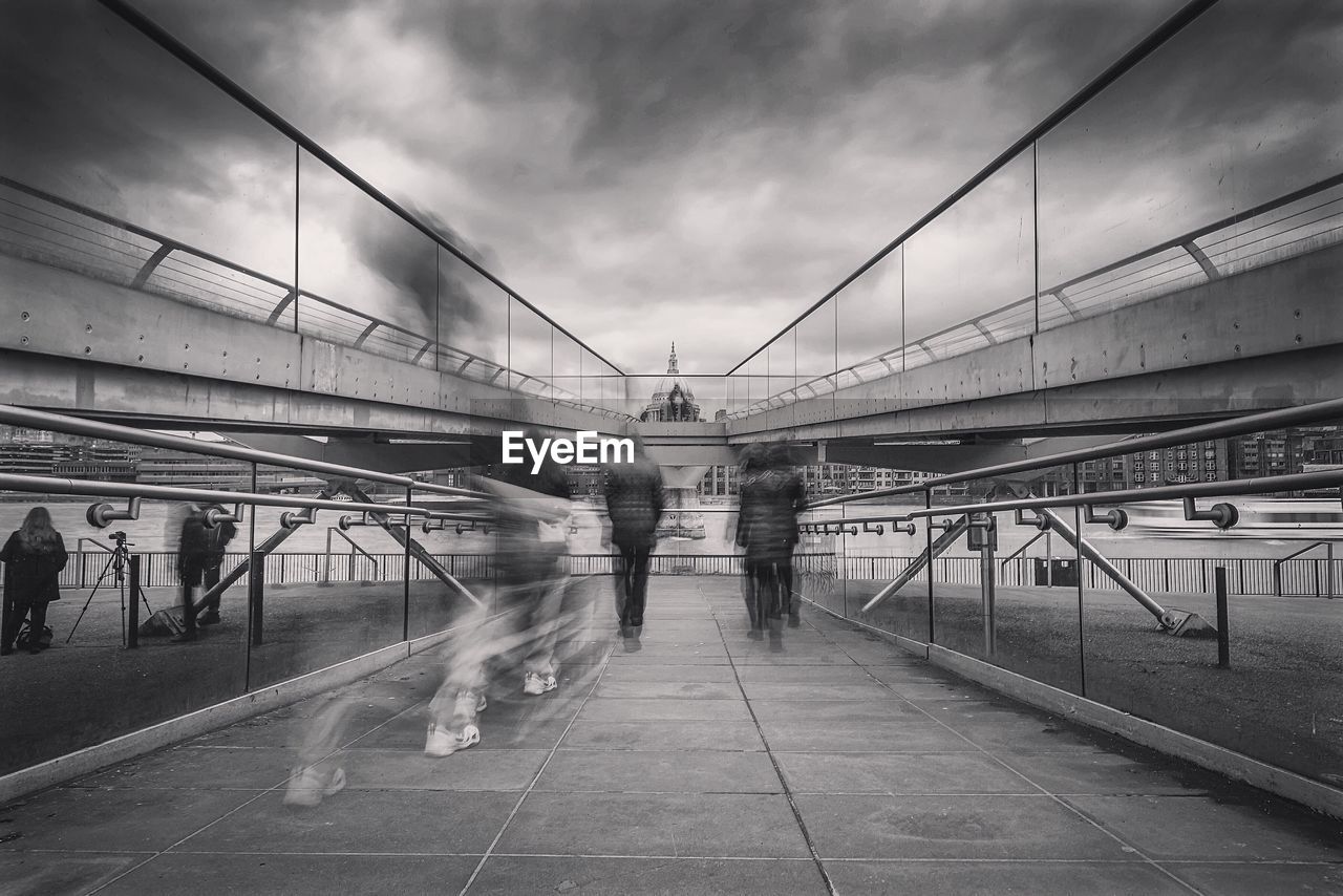 Blurred image of people walking on millennium bridge against cloudy sky