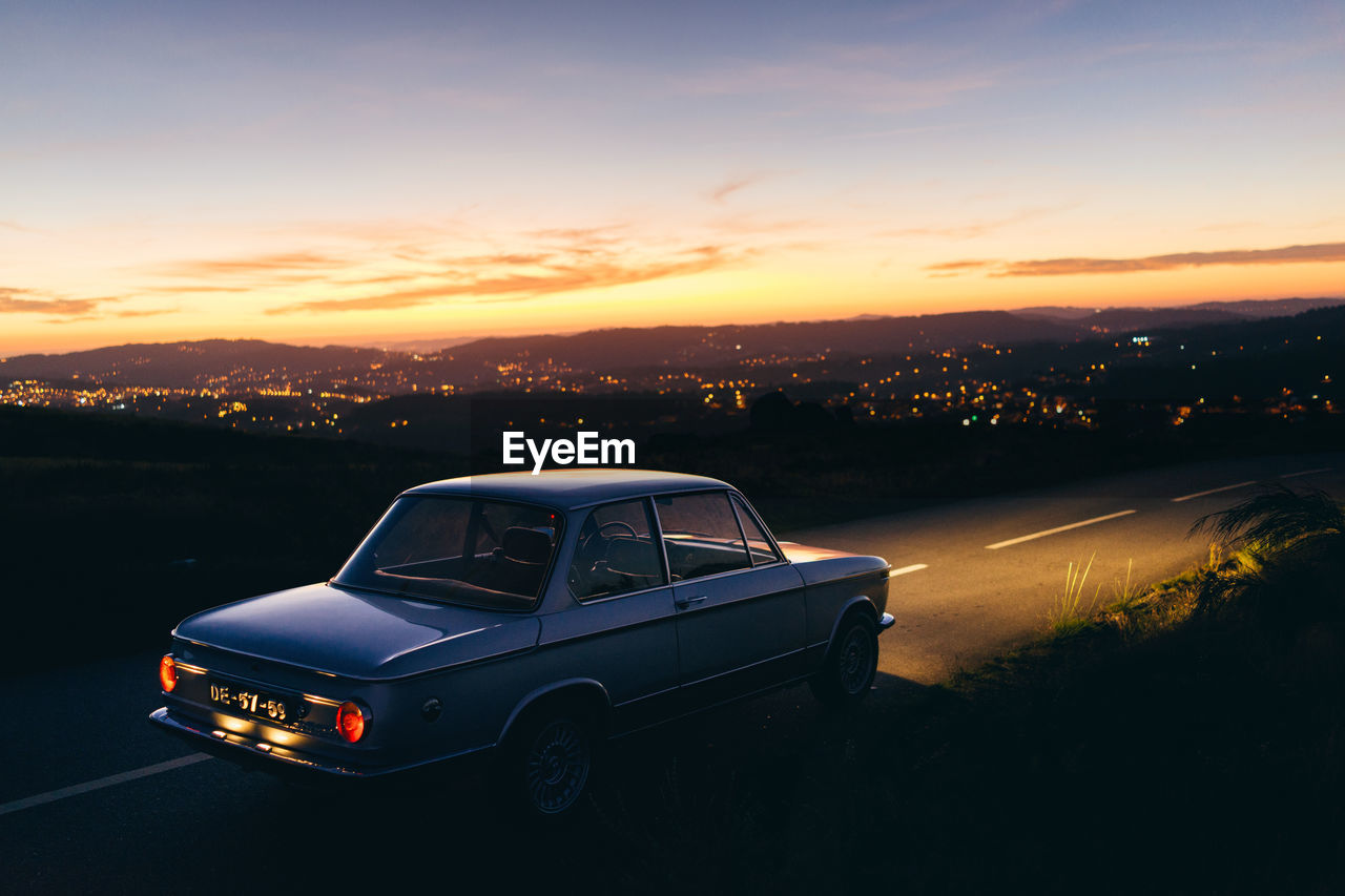 CAR ON ROAD IN CITY DURING SUNSET