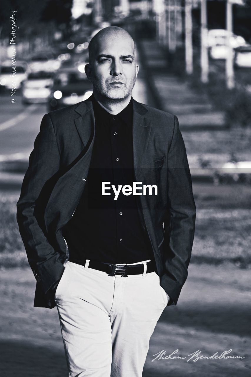 FULL LENGTH PORTRAIT OF YOUNG MAN STANDING AGAINST BLURRED BACKGROUND