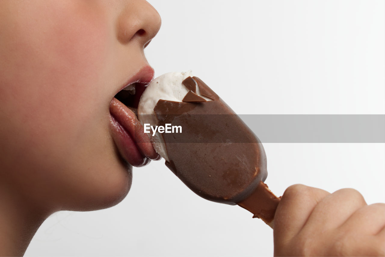 Close-up of girl eating ice cream against white background