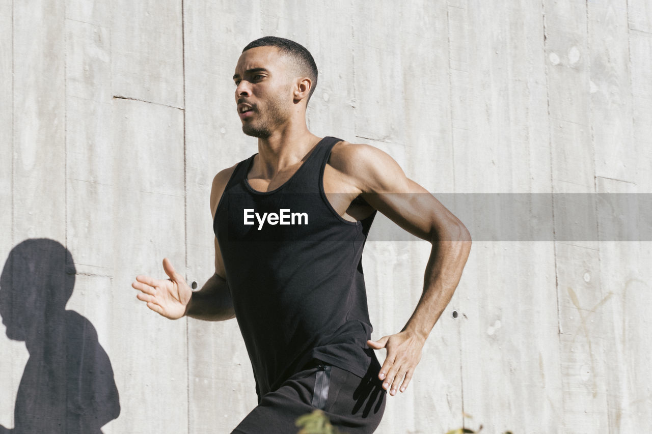 Upper part african american male athlete running against concrete wall person