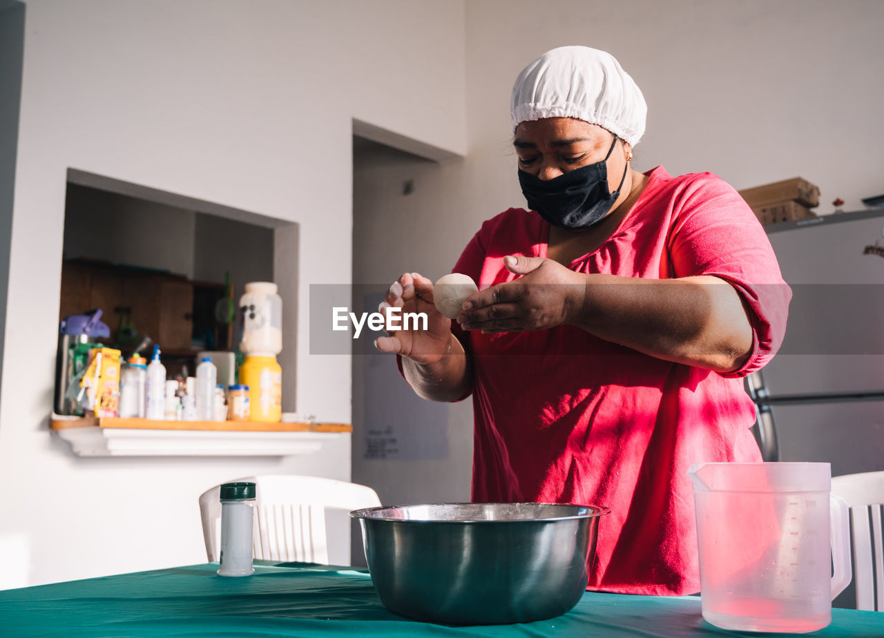 Venezuelan female in cloth face mask preparing arepas at table with bowl at home