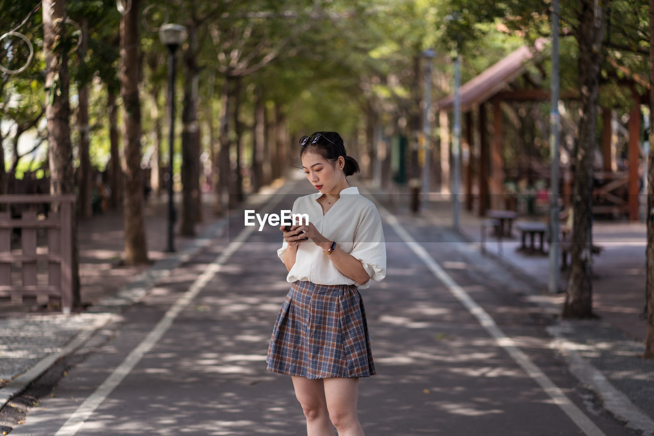 Ethnic asian female using smartphone and walking along tanya shen green bikeway in taichung