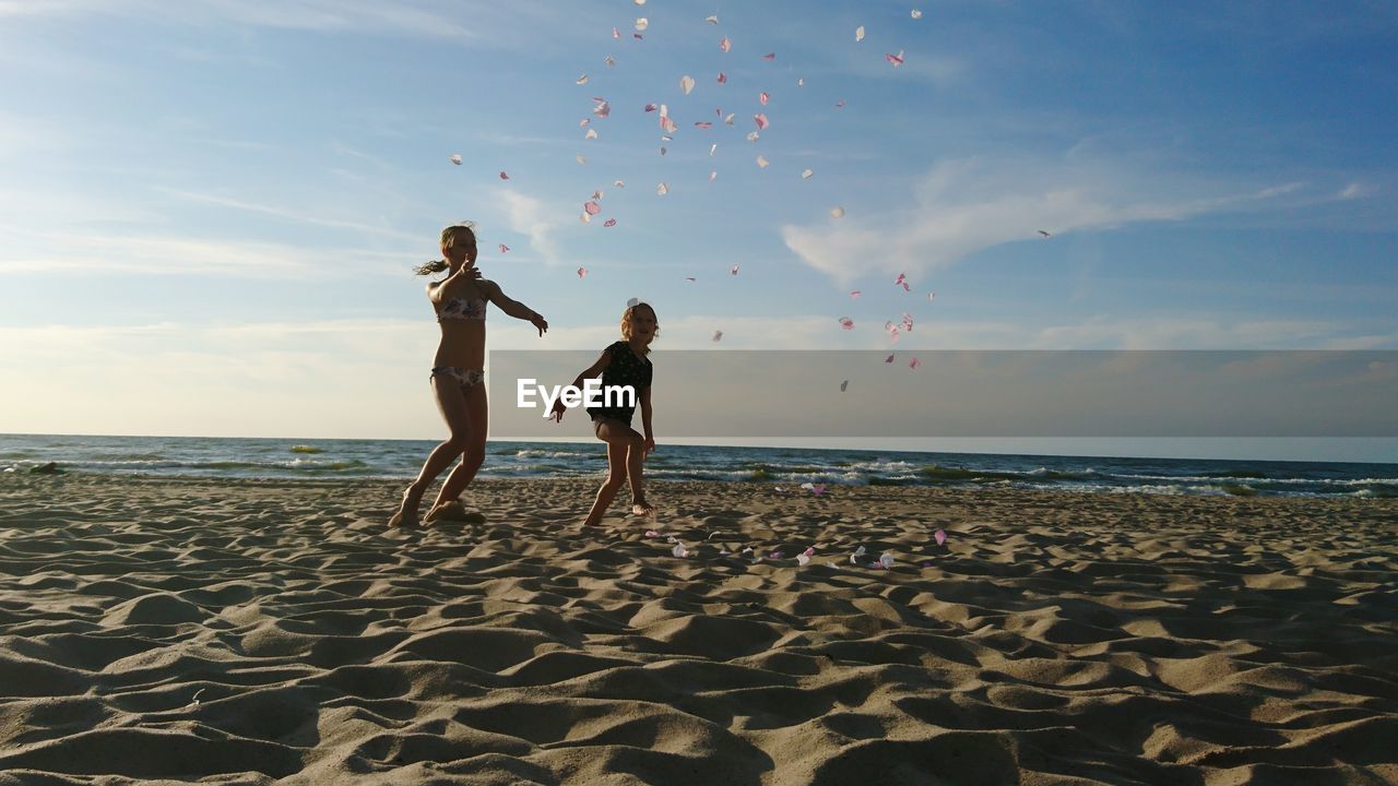 Full length of girls playing at beach against sky