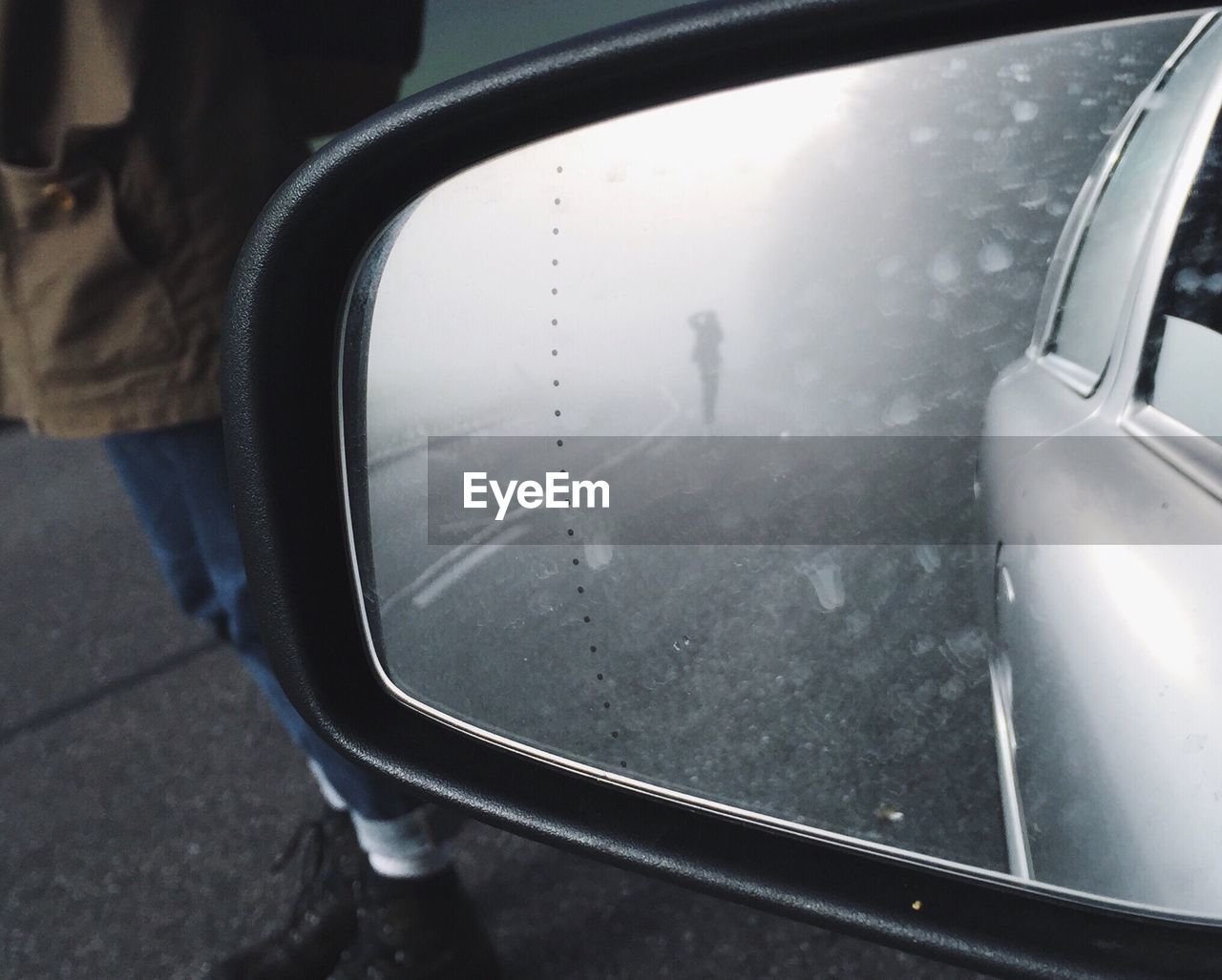 Man standing by side-view mirror of car